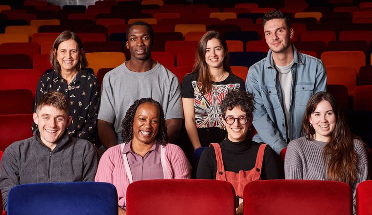 Eight people sat in the Oxford Playhouse auditorium smiling forward. Four people sit on the back row of chairs with four in front