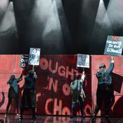 4 people hold signs in the air, another person raises their fist in the air.