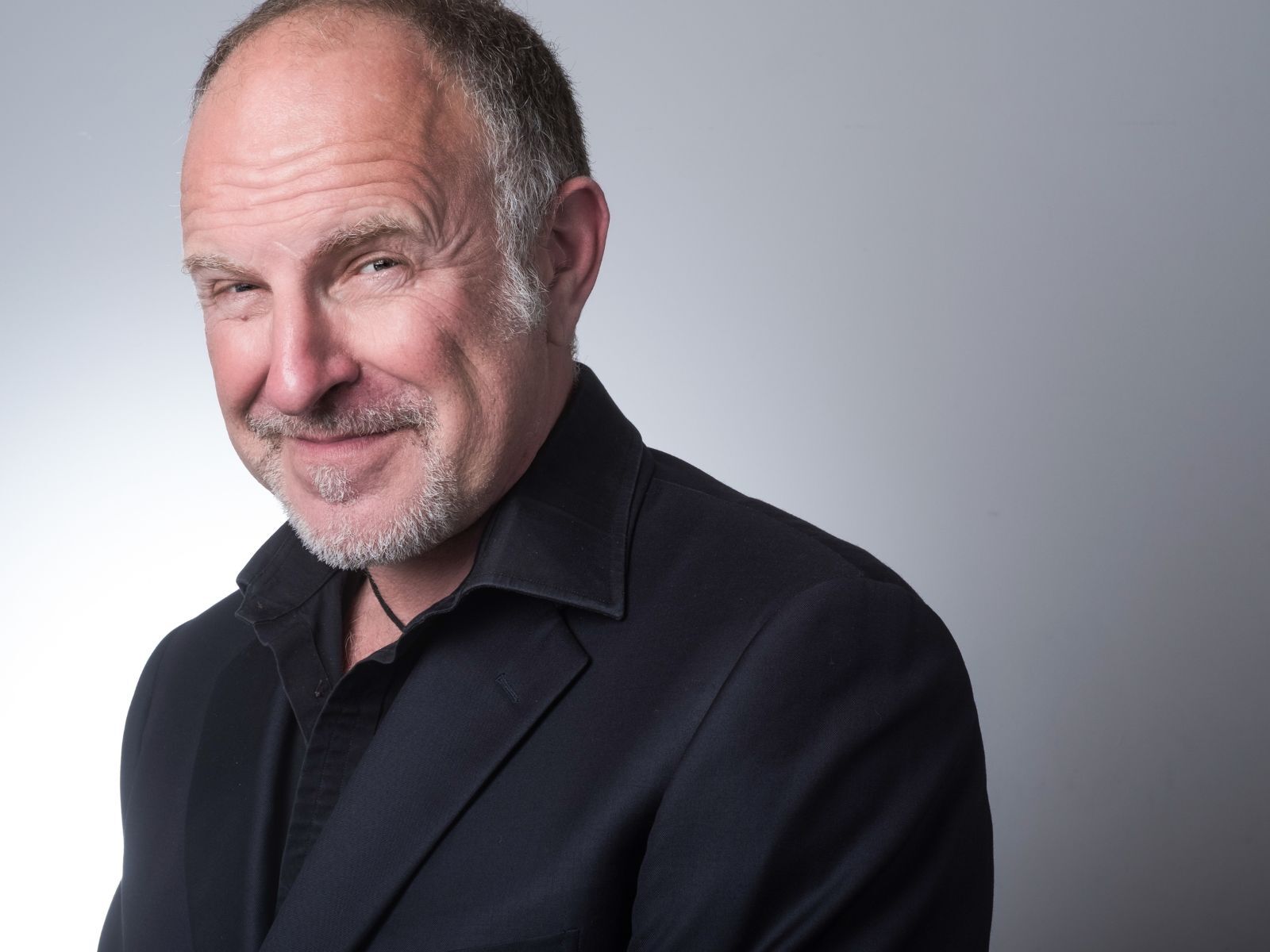 Profile photo of comedian Simon Evans in a dark suit against a grey backdrop.