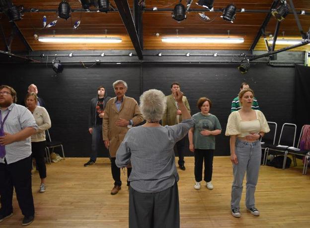 An image of a group being led through a vocal exercise with a lady at the front facing towards the participants with one hand raised in the air