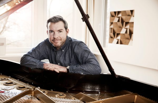 A performer leaning against a grand piano