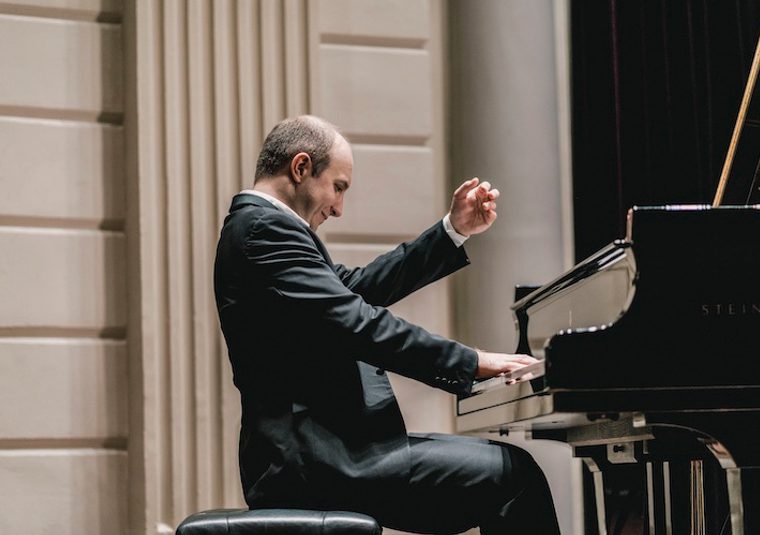 The performer playing an instrument in front of an ornate wall