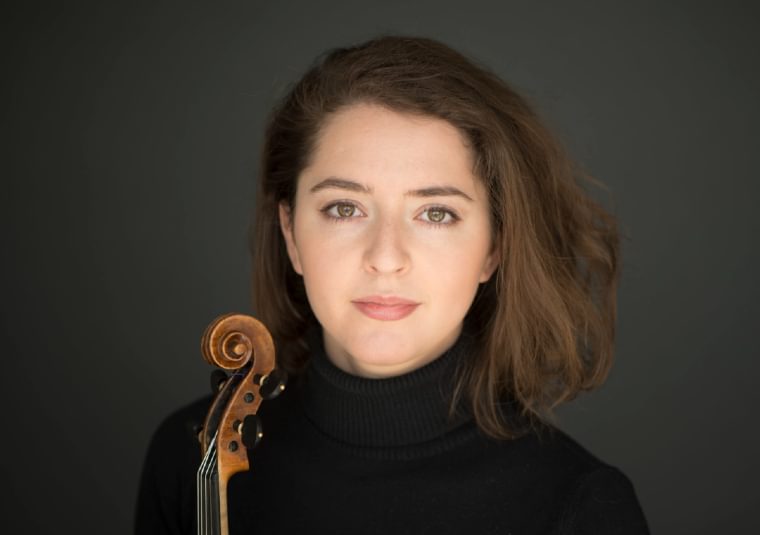 The performer holding her instrument against a dark background
