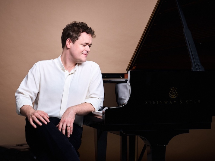 The performer standing beside a grand piano