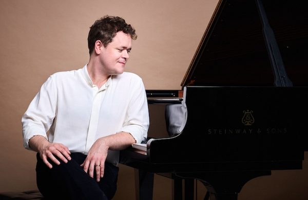 The performer standing beside a grand piano