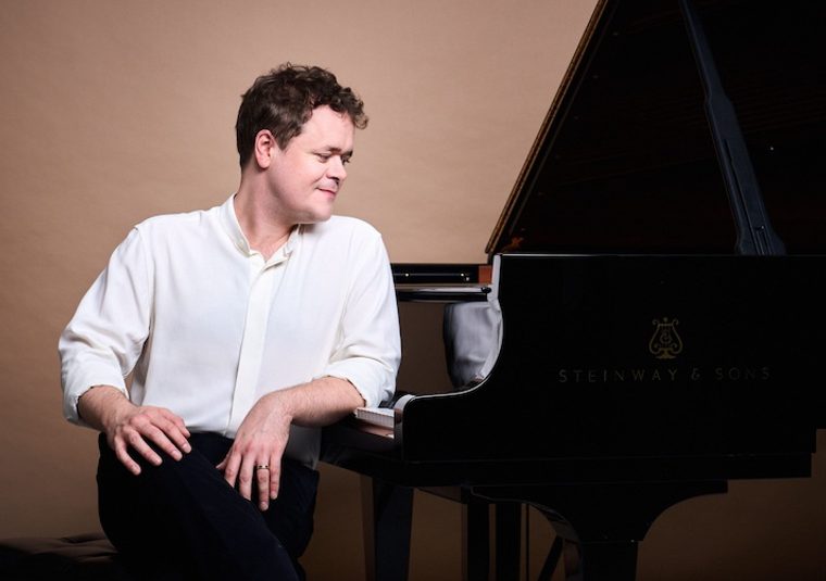 The performer standing beside a grand piano