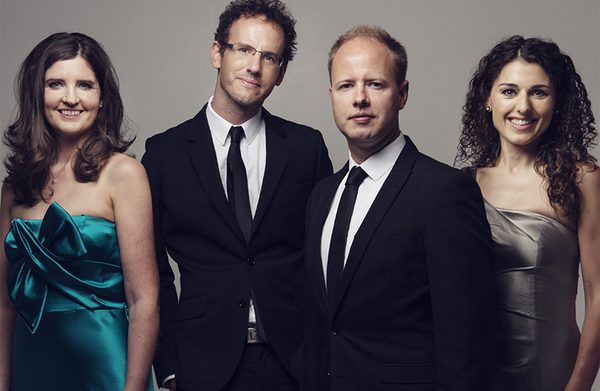 The performers standing against a gray background and looking at the camera