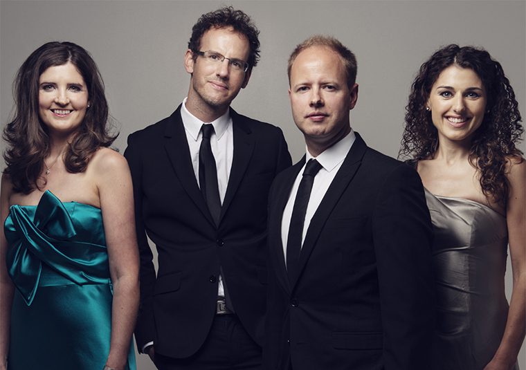 The performers standing against a gray background and looking at the camera