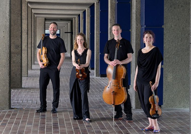The performers standing on a tiled walkway, some of them holding instruments, and facing the camera