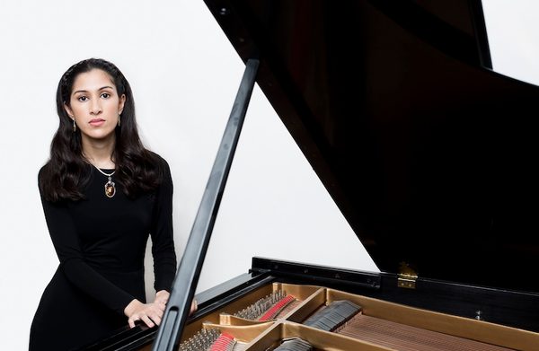 The performer standing next to an open grand piano