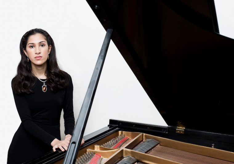 The performer standing next to an open grand piano