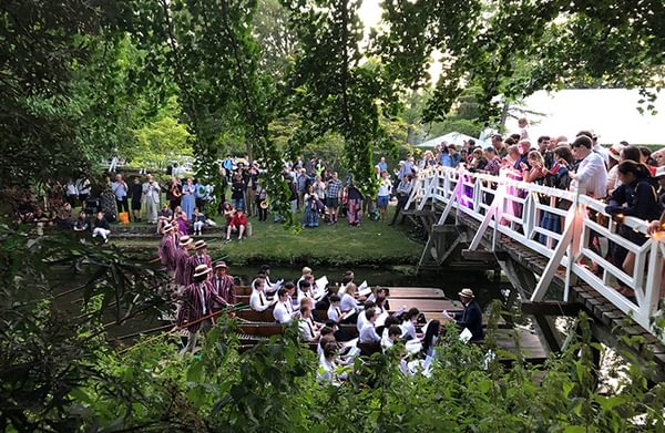 An audience gathered on a bridge and a river bank