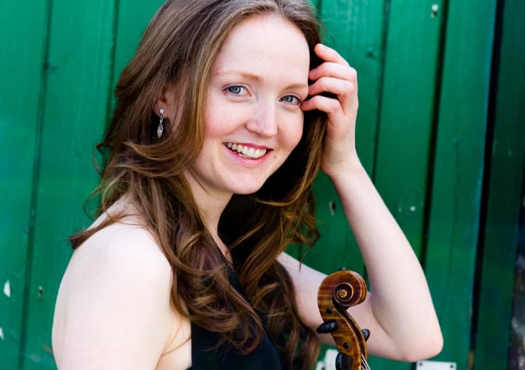 Performer standing in front of a green fence looking at the camera and smiling