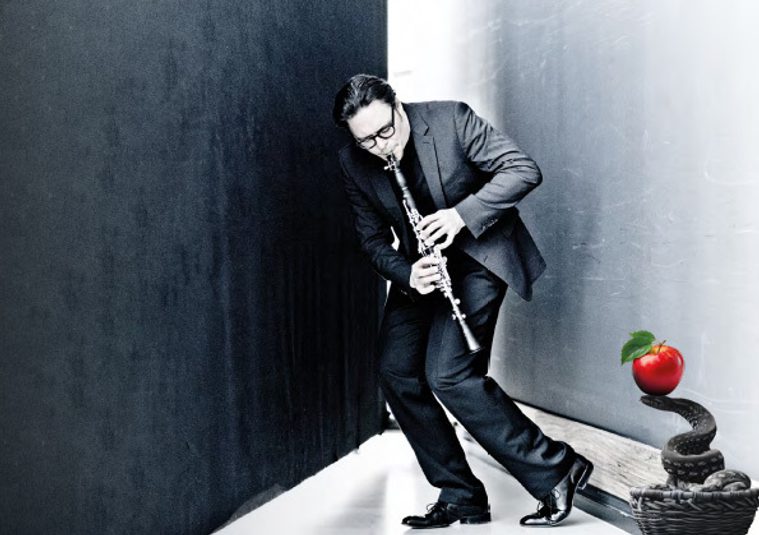 The performer holding an instrument in the corner of a room, next to a sculpture with an apple on top of it