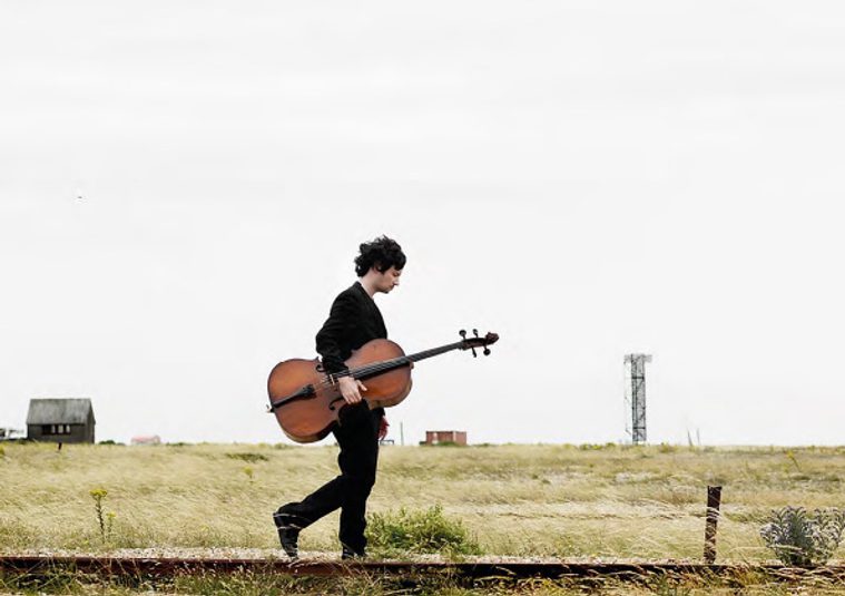The performer walking through a plain landscape holding an instrument