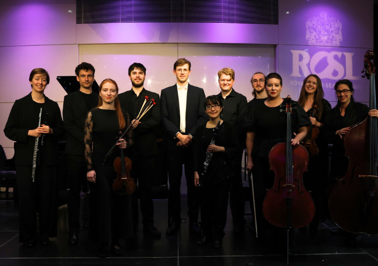 The performers, holding their instruments, and depicted in front of a white and purple backdrop