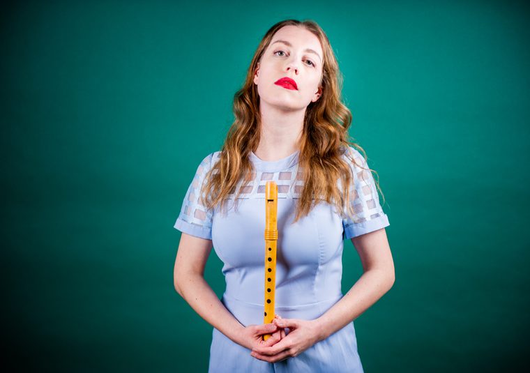 Performer holding an instrument, in front of a green background