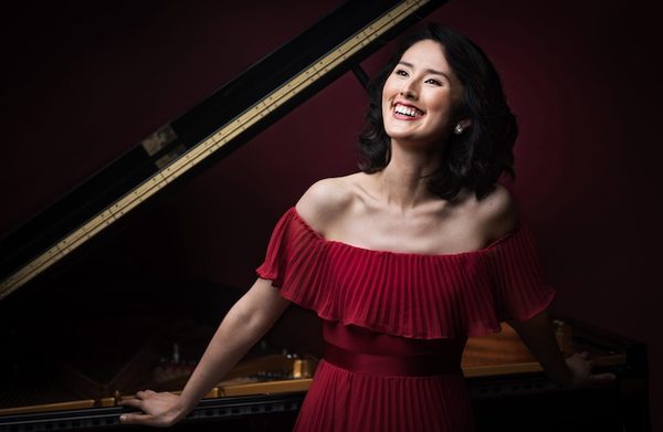 The performer standing beside a grand piano