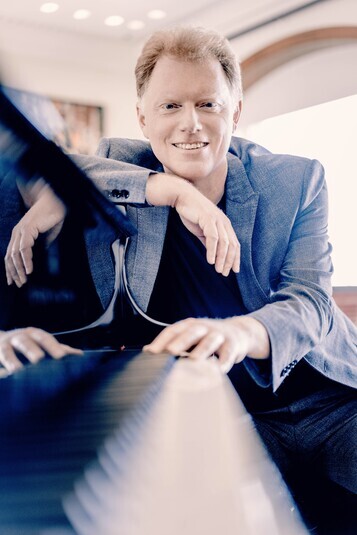 The performer sitting beside a piano looking at the camera